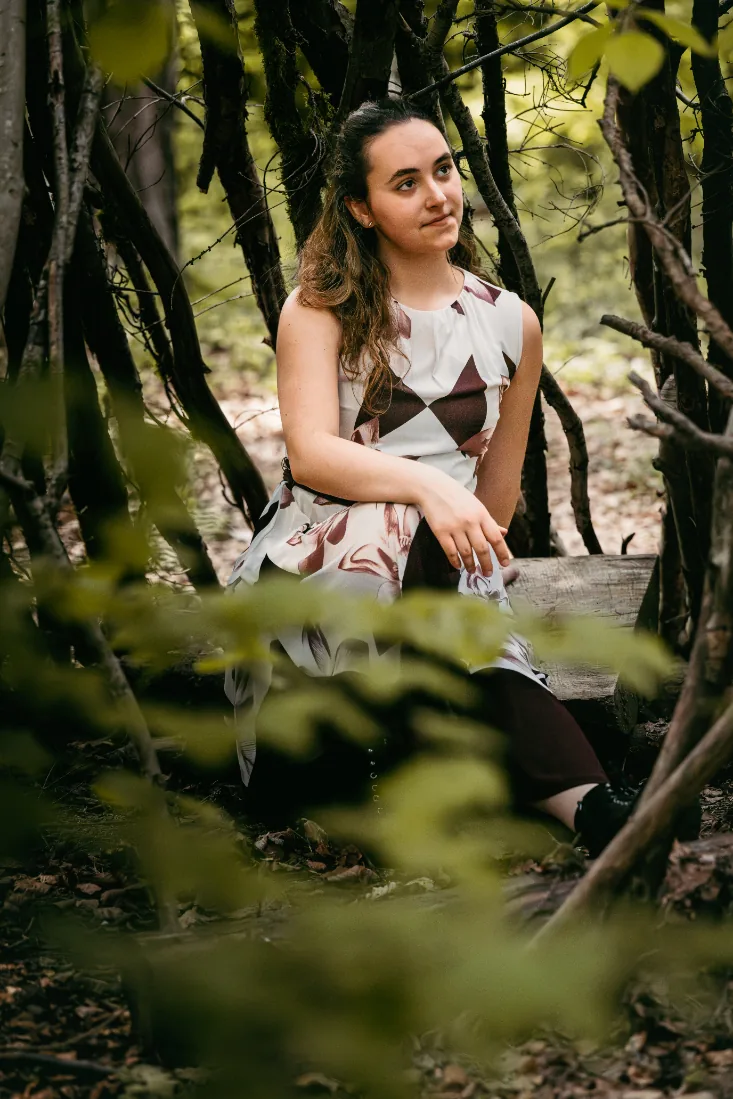 Frau sitzt auf einem Baumstamm im Wald und blickt zur Seite, natürliche Porträtfotografie